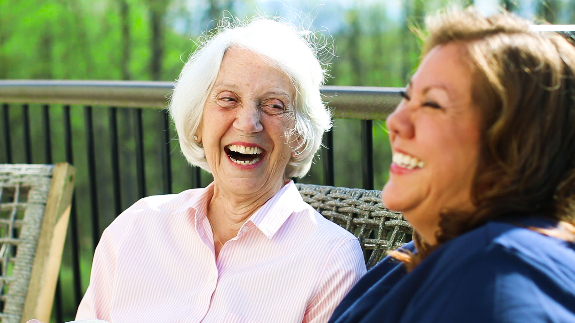 female Home care giver laughing with elderly female client as they sit outside